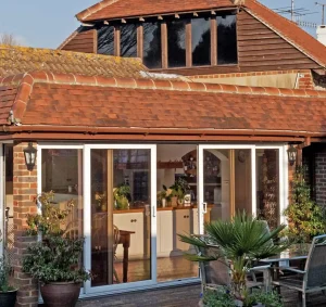 White uPVC patio sliding doors installed on a house with an orangish brown roof, decorated by green plants.