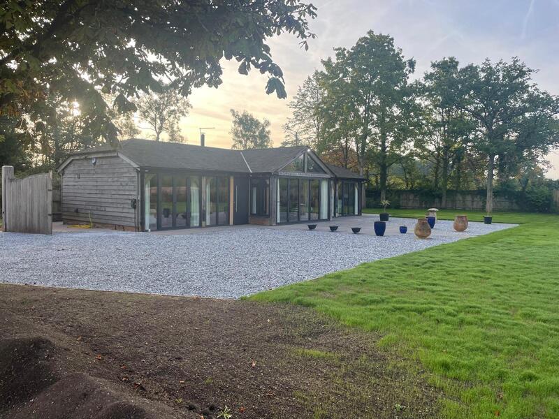 Modern RAL 7016 aluminium bi-fold doors with flush thresholds integrated into a
weathered timber-framed barn extension.